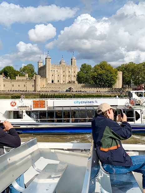 Sightseeing cruise passengers view the Tower of London from the Thames River.