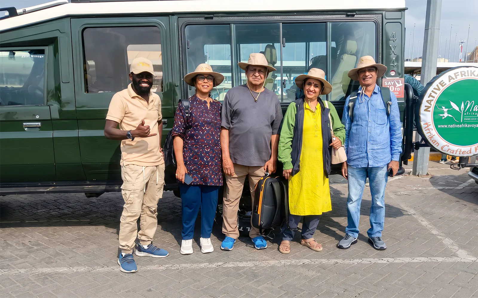 Group of tourists ready for 5-day Kiboko safari, standing by a safari vehicle.