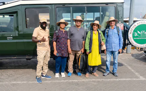 Group of tourists ready for 5-day Kiboko safari, standing by a safari vehicle.