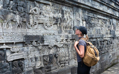 Backpacker admiring stone carvings at Borobudur Temple, Java, Indonesia.