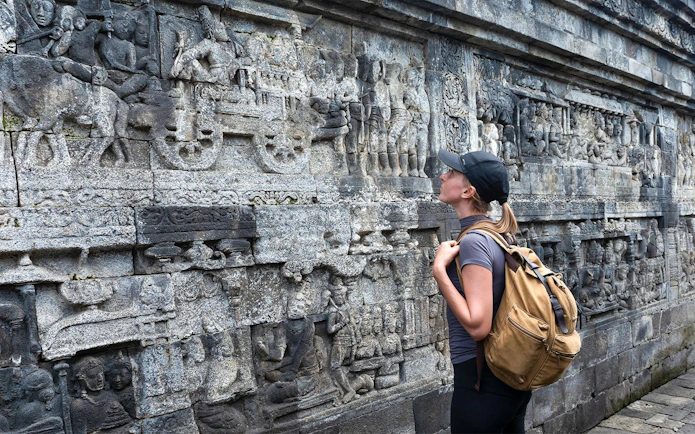 Backpacker admiring stone carvings at Borobudur Temple, Java, Indonesia.