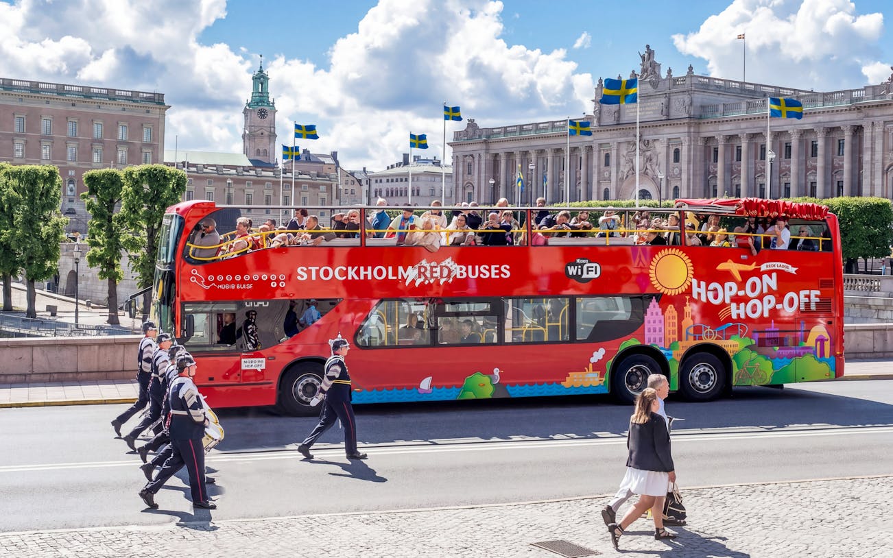 Stockholm hop-on hop-off bus near Royal Palace with tourists on top deck.