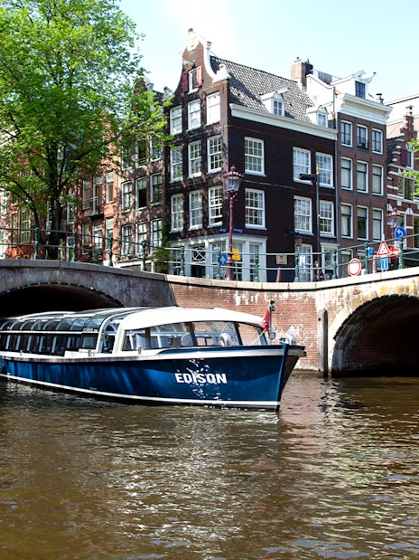 Canal boat under bridge in Amsterdam near STRAAT Museum.