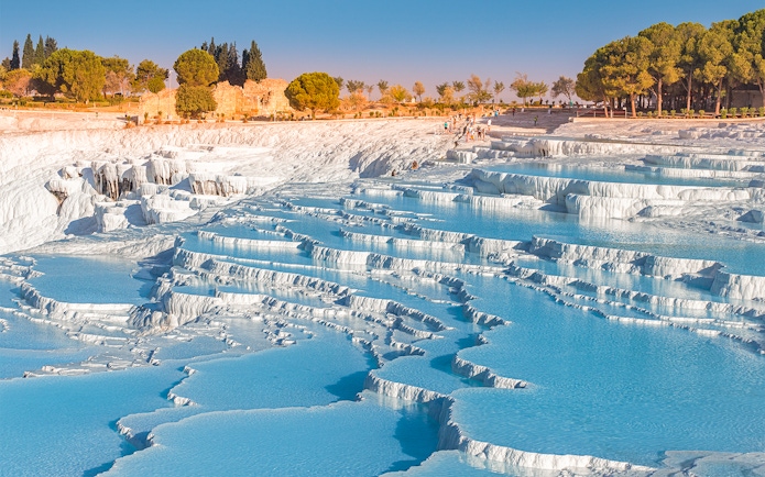 Terraced thermal pools at Pamukkale, Turkey, with limestone formations and tourists exploring.