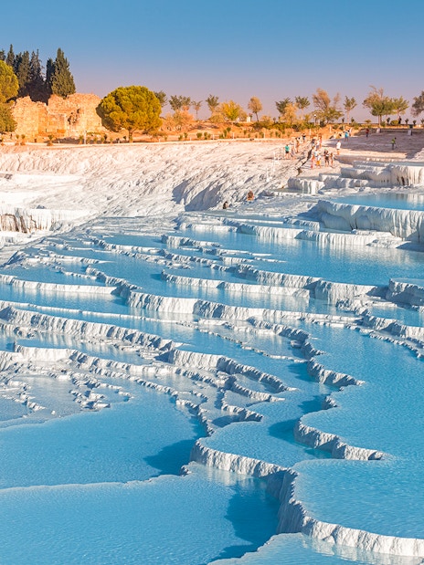 Terraced thermal pools at Pamukkale, Turkey, with limestone formations and tourists exploring.