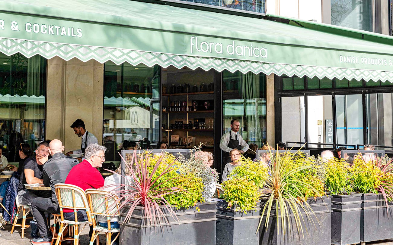 Outdoor breakfast seating at Flora Danica with patrons dining under a green awning.