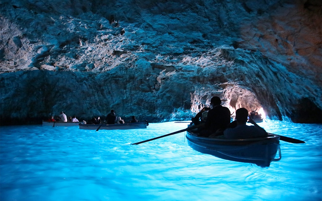 Boats entering the illuminated Blue Grotto cave in Capri, Italy.
