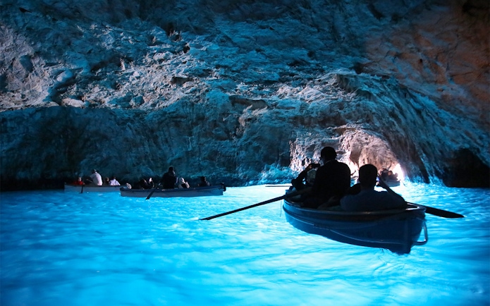 Boats entering the illuminated Blue Grotto cave in Capri, Italy.