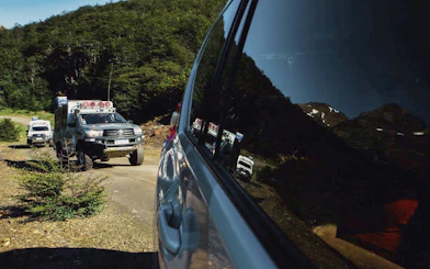 Off-road 4x4 vehicles on a dirt trail near Lakes Escondido and Fagnano, surrounded by forest.