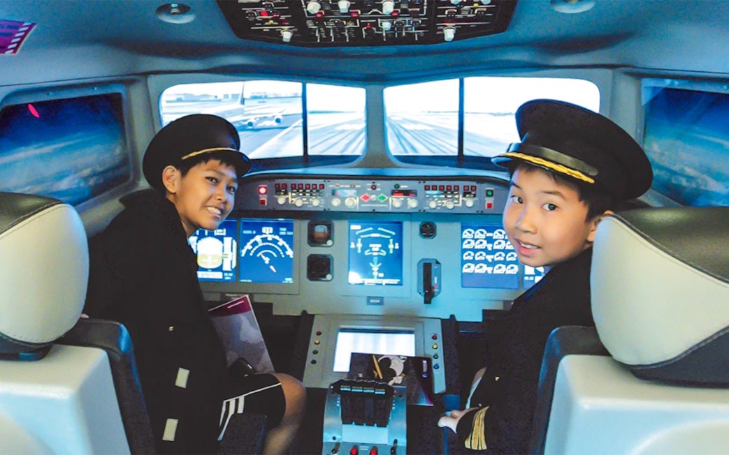 Kids in pilot uniforms in airplane cockpit simulator at KidZania.