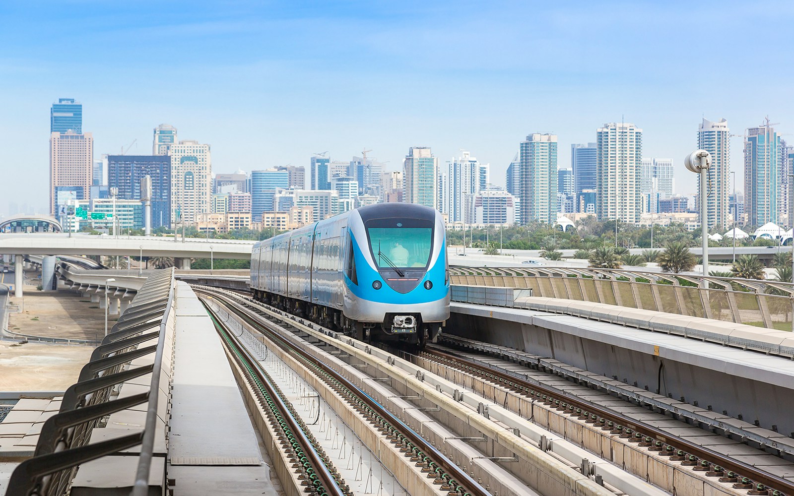 Dubai Metro train on elevated tracks with city skyline in the background.