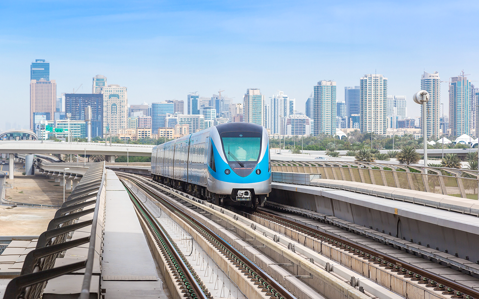 Dubai Metro train on elevated tracks with city skyline in the background.
