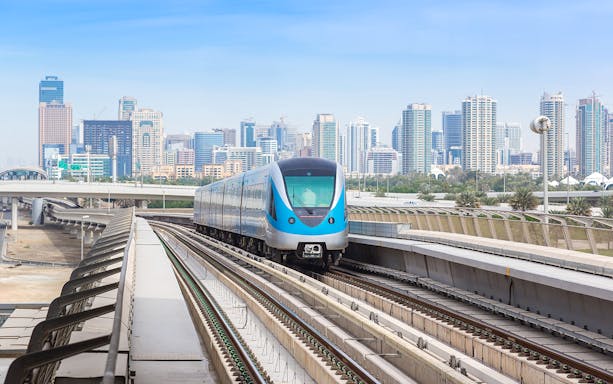 Dubai Metro train on elevated tracks with city skyline in the background.