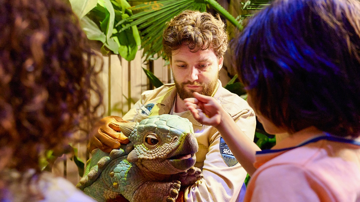 trainer and tourists interacting with little dinosaur