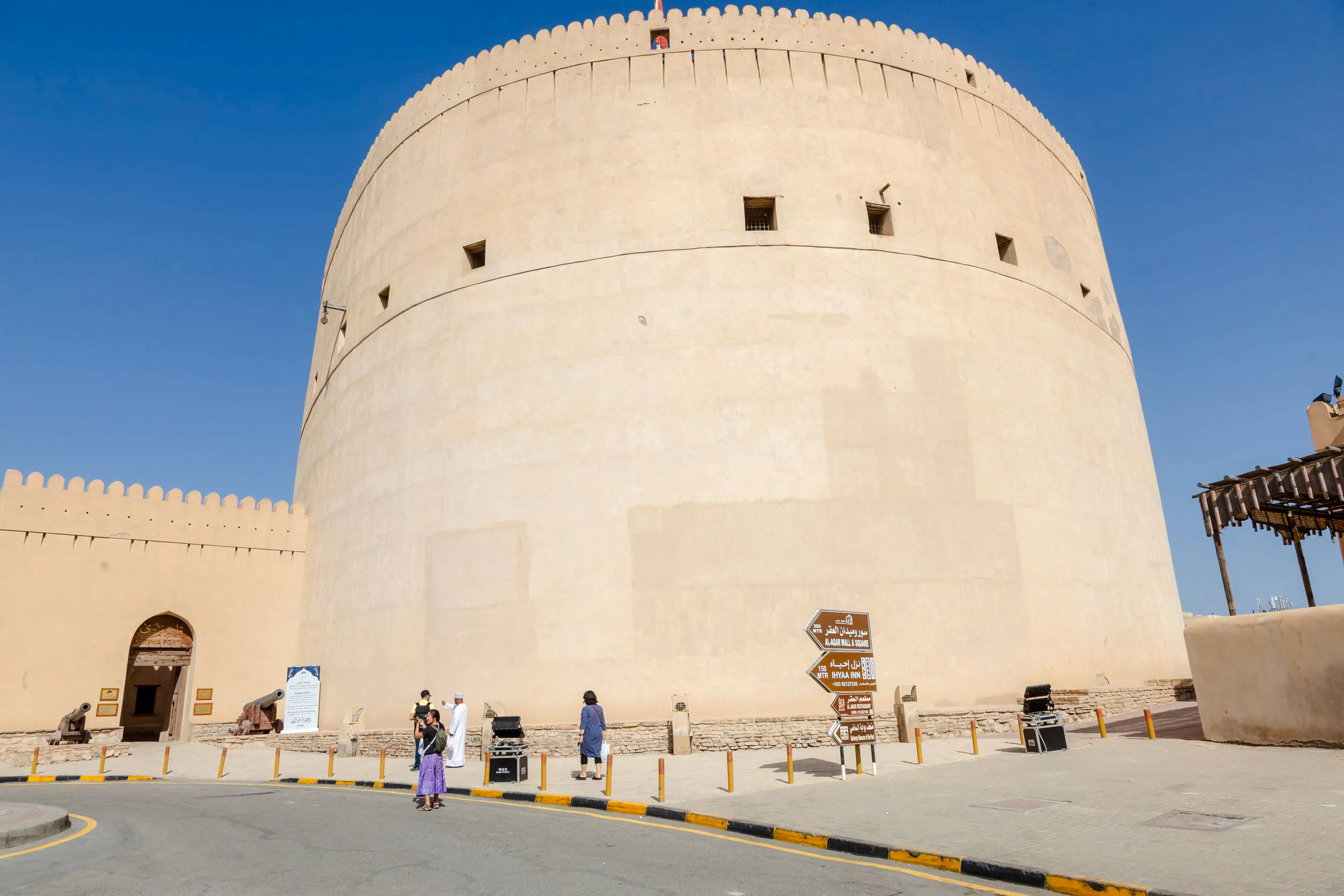 Nizwa Fort with visitors and directional signs, part of the Muscat to Nizwa historical tour.