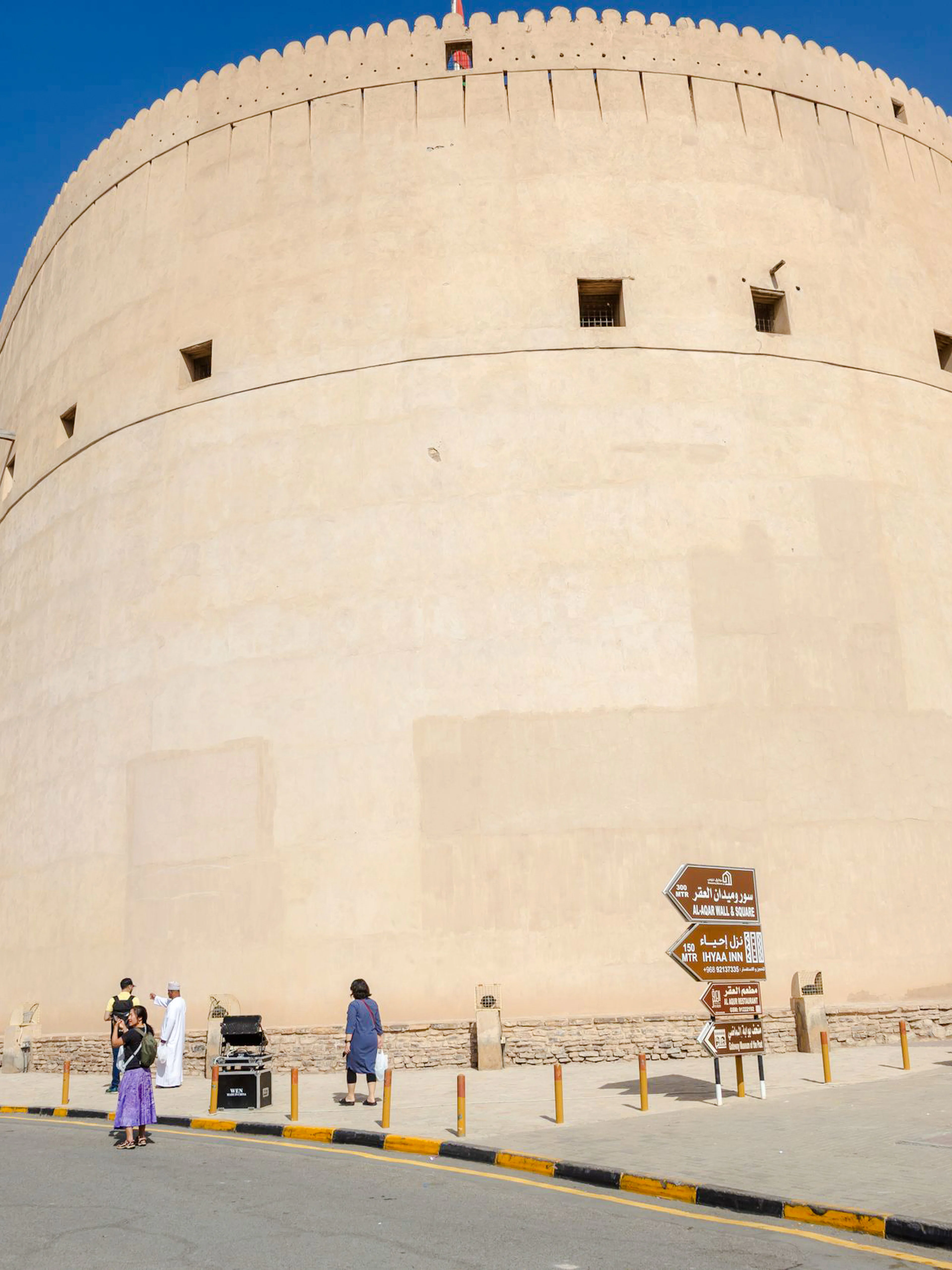 Nizwa Fort with visitors and directional signs, part of the Muscat to Nizwa historical tour.