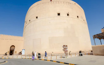 Nizwa Fort with visitors and directional signs, part of the Muscat to Nizwa historical tour.