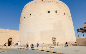 Nizwa Fort with visitors and directional signs, part of the Muscat to Nizwa historical tour.