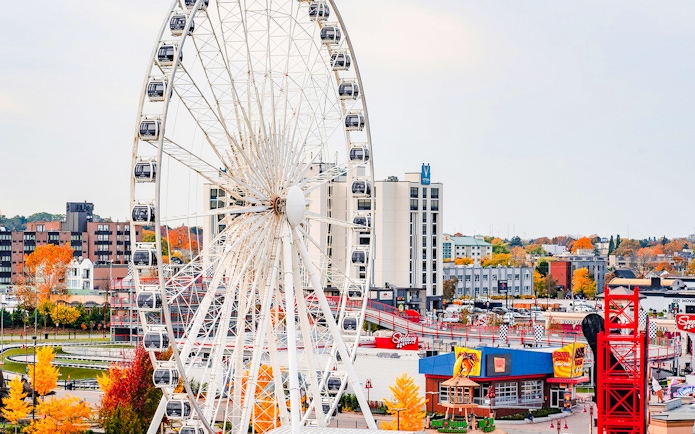 Ferris wheel at Niagara Falls with cityscape and autumn trees.