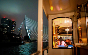 Cruise boat dining with view of Erasmus Bridge in Rotterdam at night.