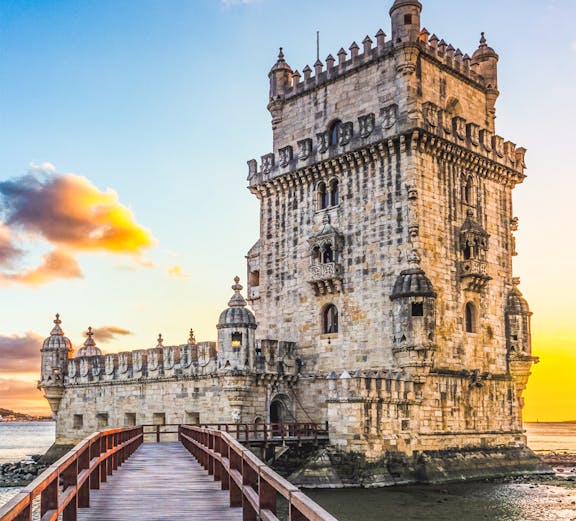 Belem Tower in Lisbon at sunset with a wooden walkway leading to the historic structure.