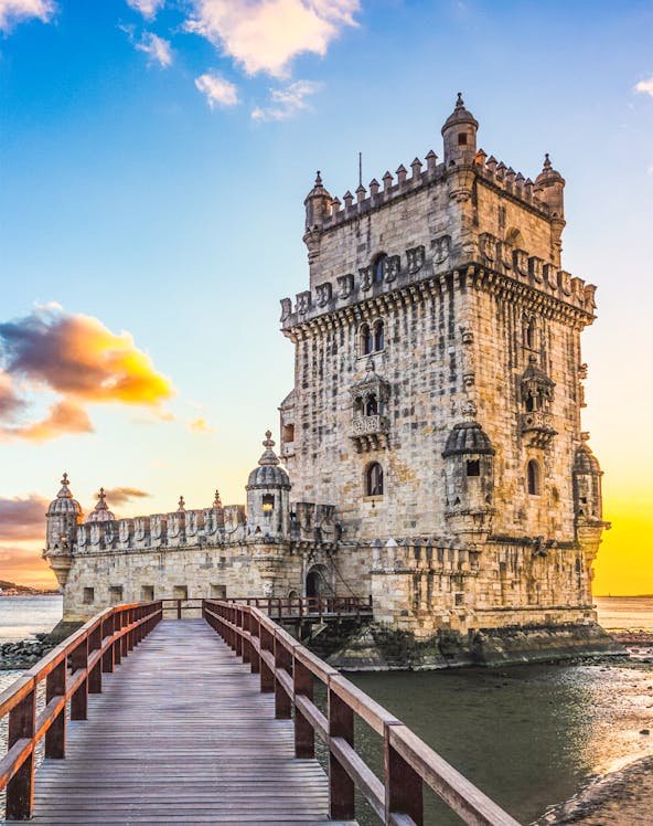 Belem Tower in Lisbon at sunset with a wooden walkway leading to the historic structure.