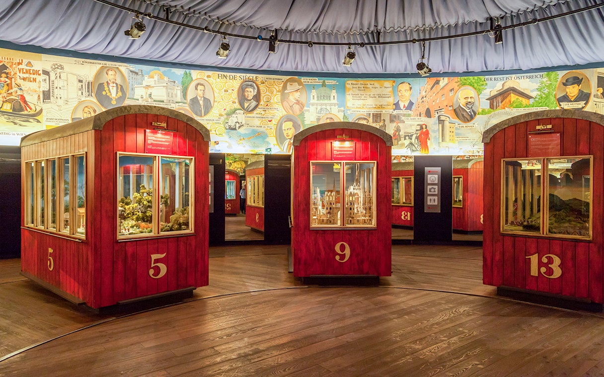 Red exhibition pods at The Wheel of History ‘Panorama’ with historical murals in the background.