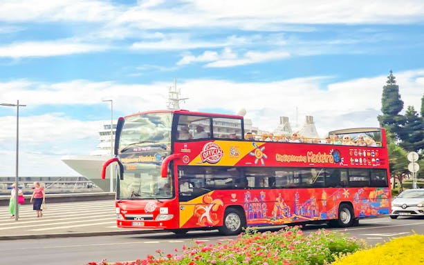 Hop-on hop-off bus tour in Funchal, Madeira, with cruise ship in background.