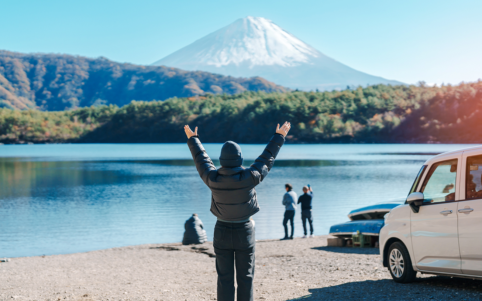 Tourist at Lake Saiko with arms raised, viewing Mount Fuji in Japan.