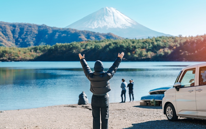 Tourist at Lake Saiko with arms raised, viewing Mount Fuji in Japan.