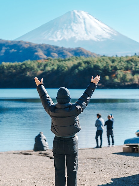 Tourist at Lake Saiko with arms raised, viewing Mount Fuji in Japan.