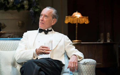 Actor in formal attire holding a glass during HAY FEVER performance, Westend.