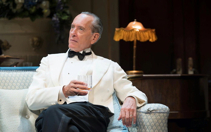Actor in formal attire holding a glass during HAY FEVER performance, Westend.