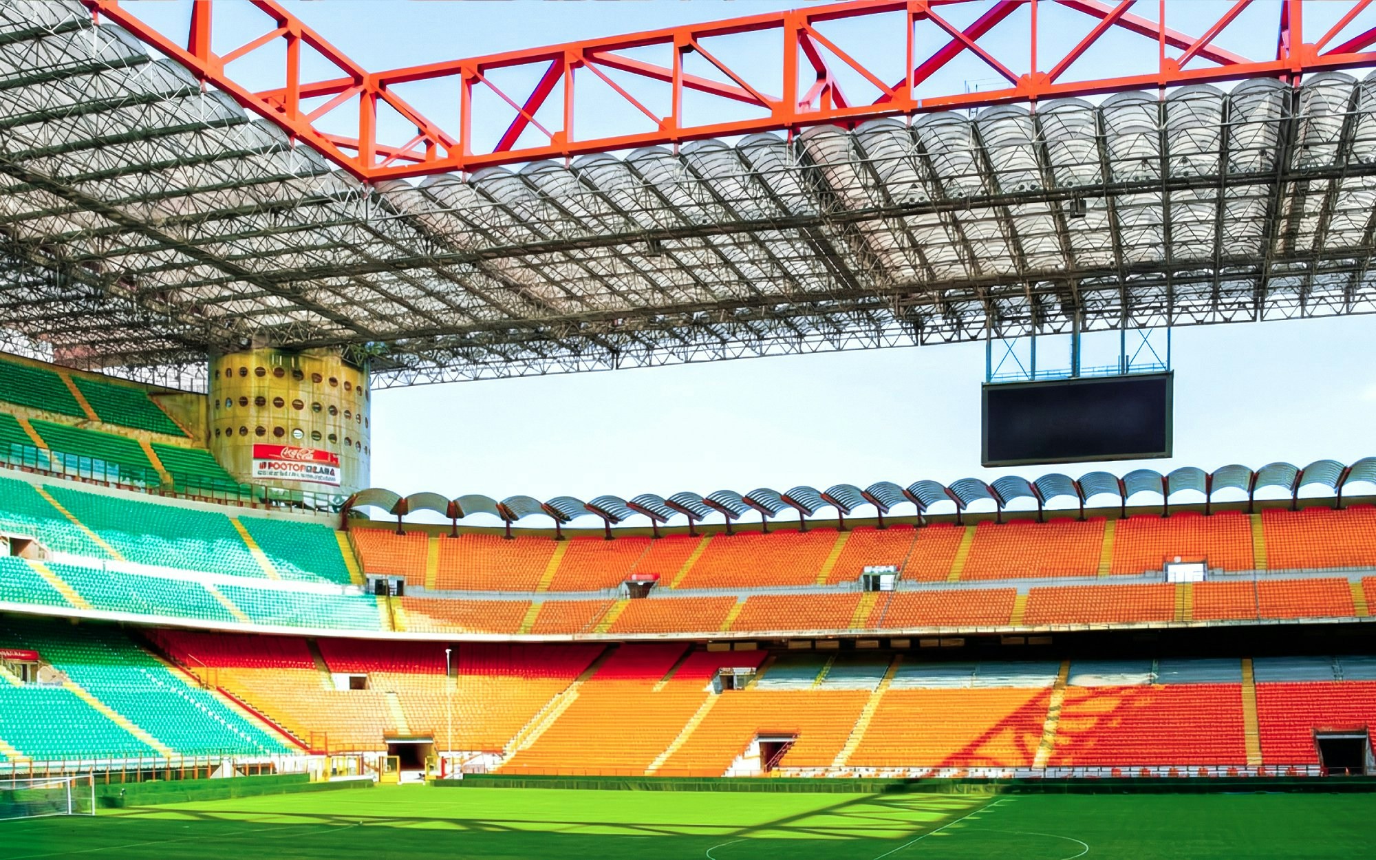 San Siro stadium field with empty colorful seats and large screen.