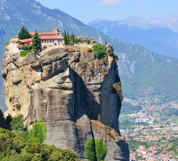 Monastery atop rock formation in Meteora, Greece, with mountainous backdrop.