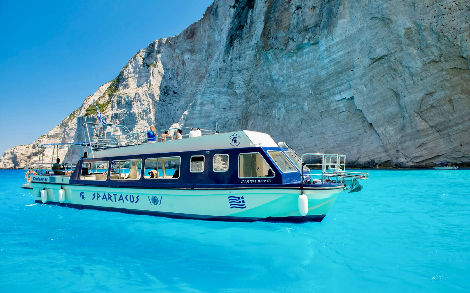 Glass bottom boat near cliffs at Shipwreck Beach, Zakynthos, during Blue Caves Land & Sea Tour.