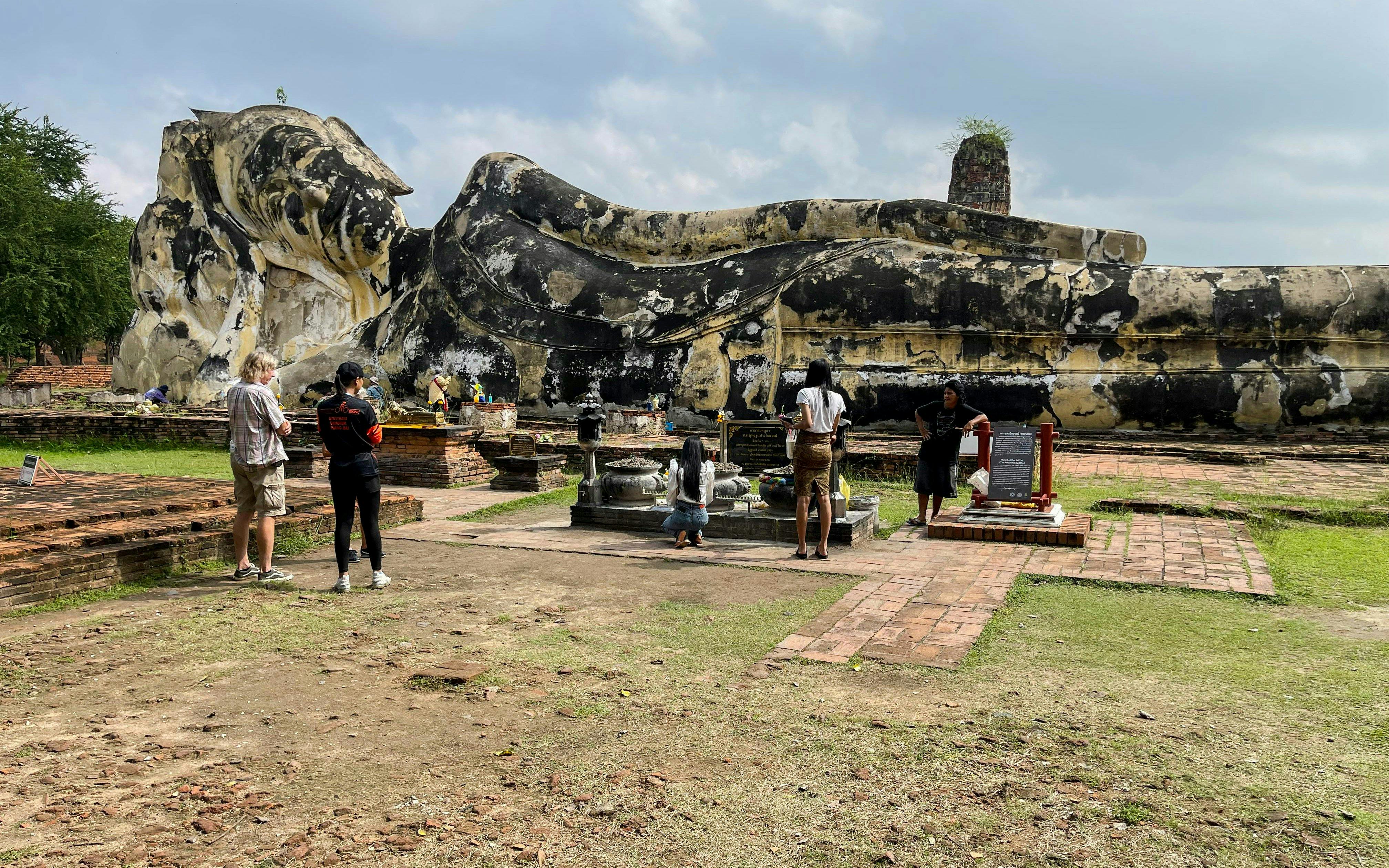 Reclining Buddha statue in Ayutthaya with visitors exploring the historic site.