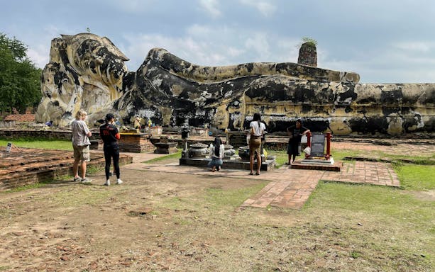Reclining Buddha statue in Ayutthaya with visitors exploring the historic site.