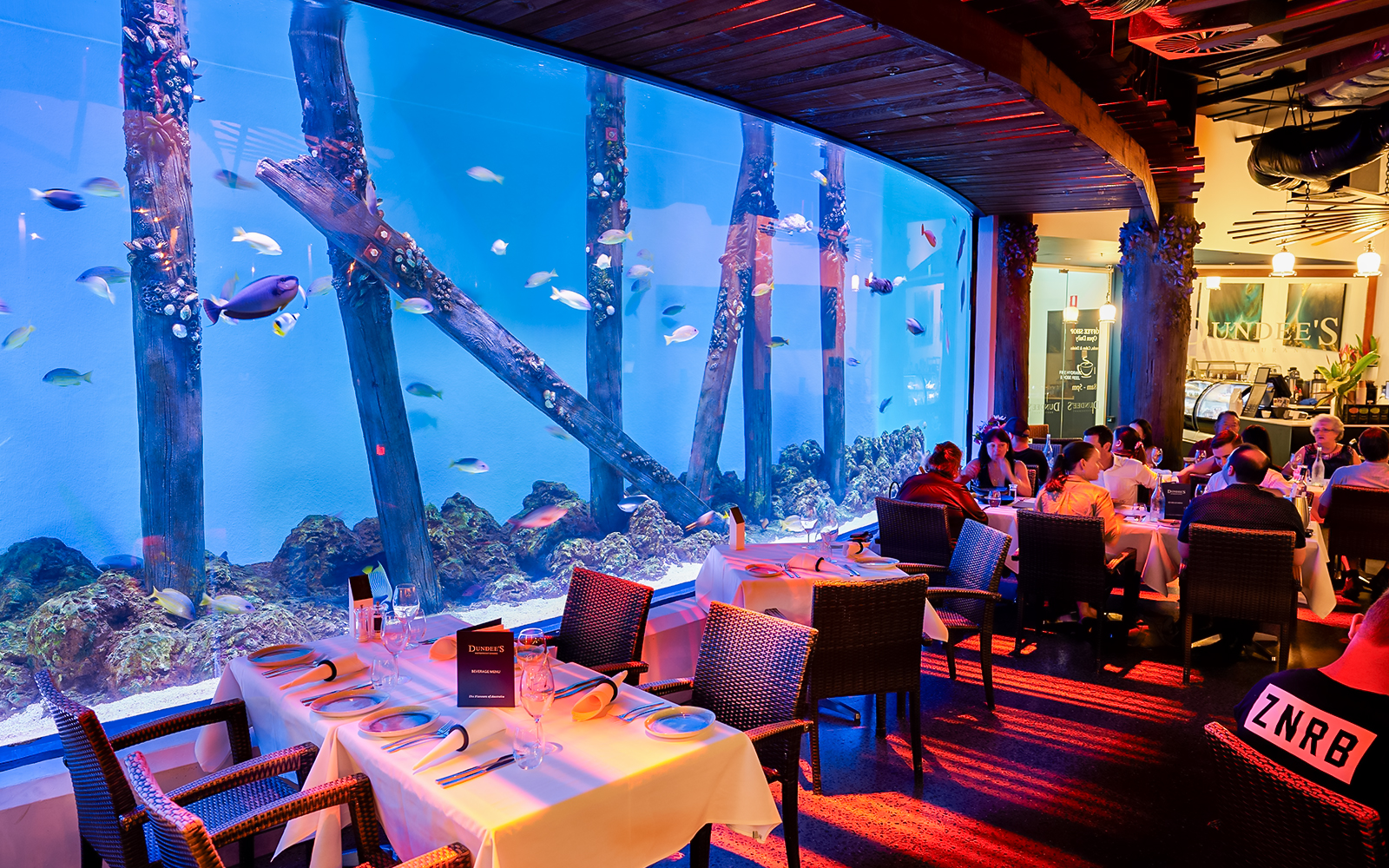 Dining area at Dundees Restaurant inside Cairns Aquarium with large fish tank at night.