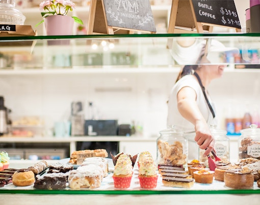 Bakery display with assorted pastries and a person serving behind the counter.