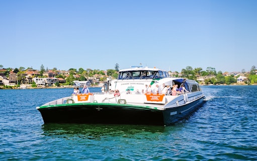 Sydney ferry on the water with passengers, cityscape in the background.