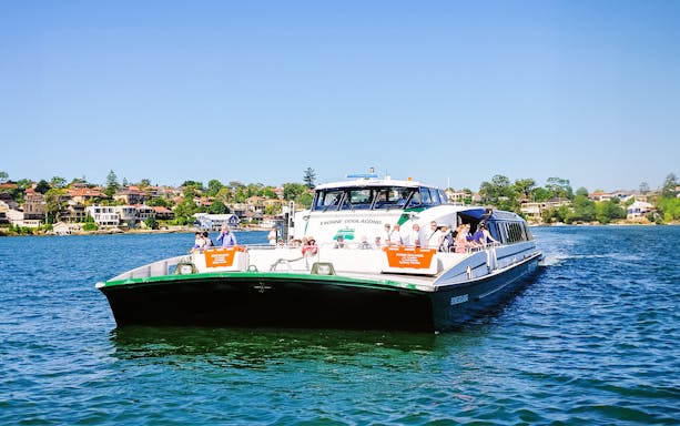 Sydney ferry on the water with passengers, cityscape in the background.