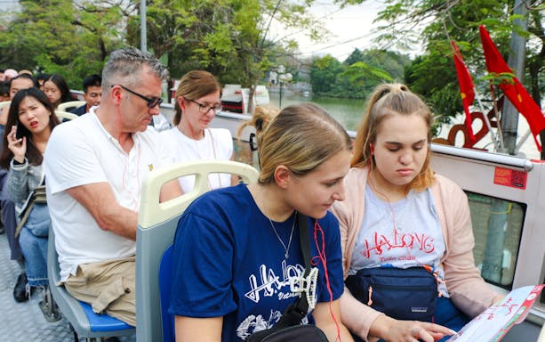 Passengers on a hop-on hop-off bus tour in Hanoi, Vietnam, looking at a map.