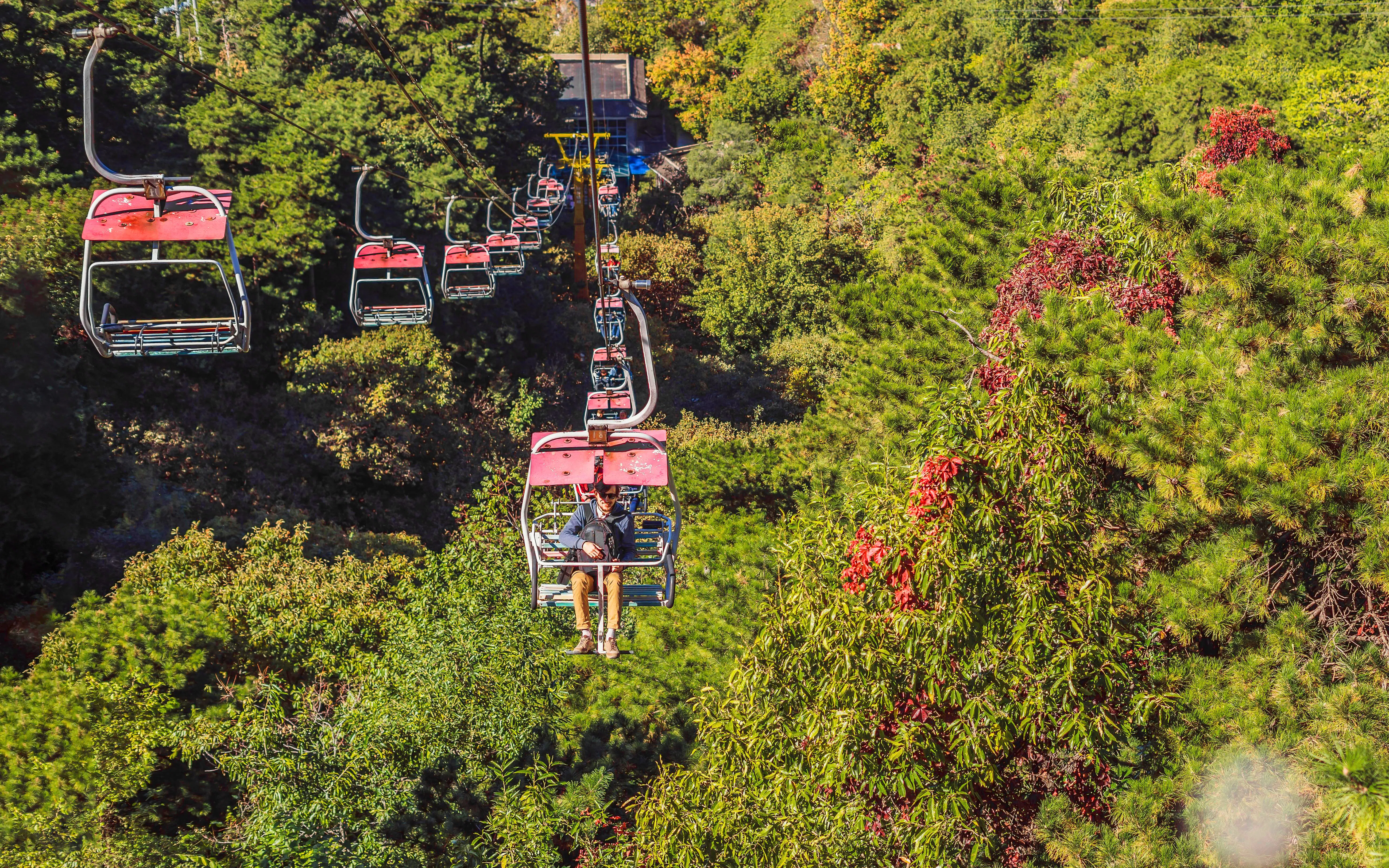 Man on cable car ascending through forest to the Great Wall of China.