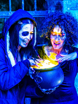 Two people in Halloween makeup gather around a glowing cauldron at a Halloween event.