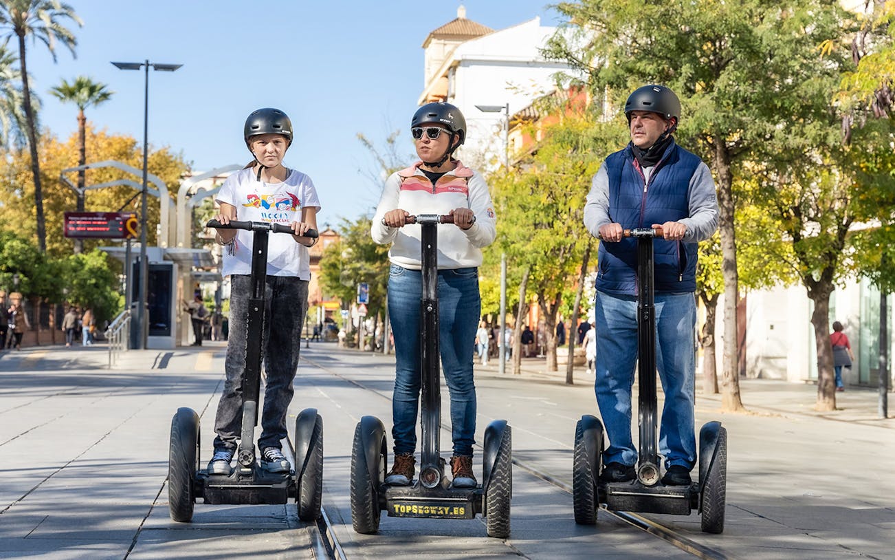 Three people riding Segways on a tree-lined street in Seville during a tour.
