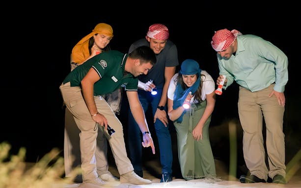 Group exploring desert at night with flashlights on a private night safari.