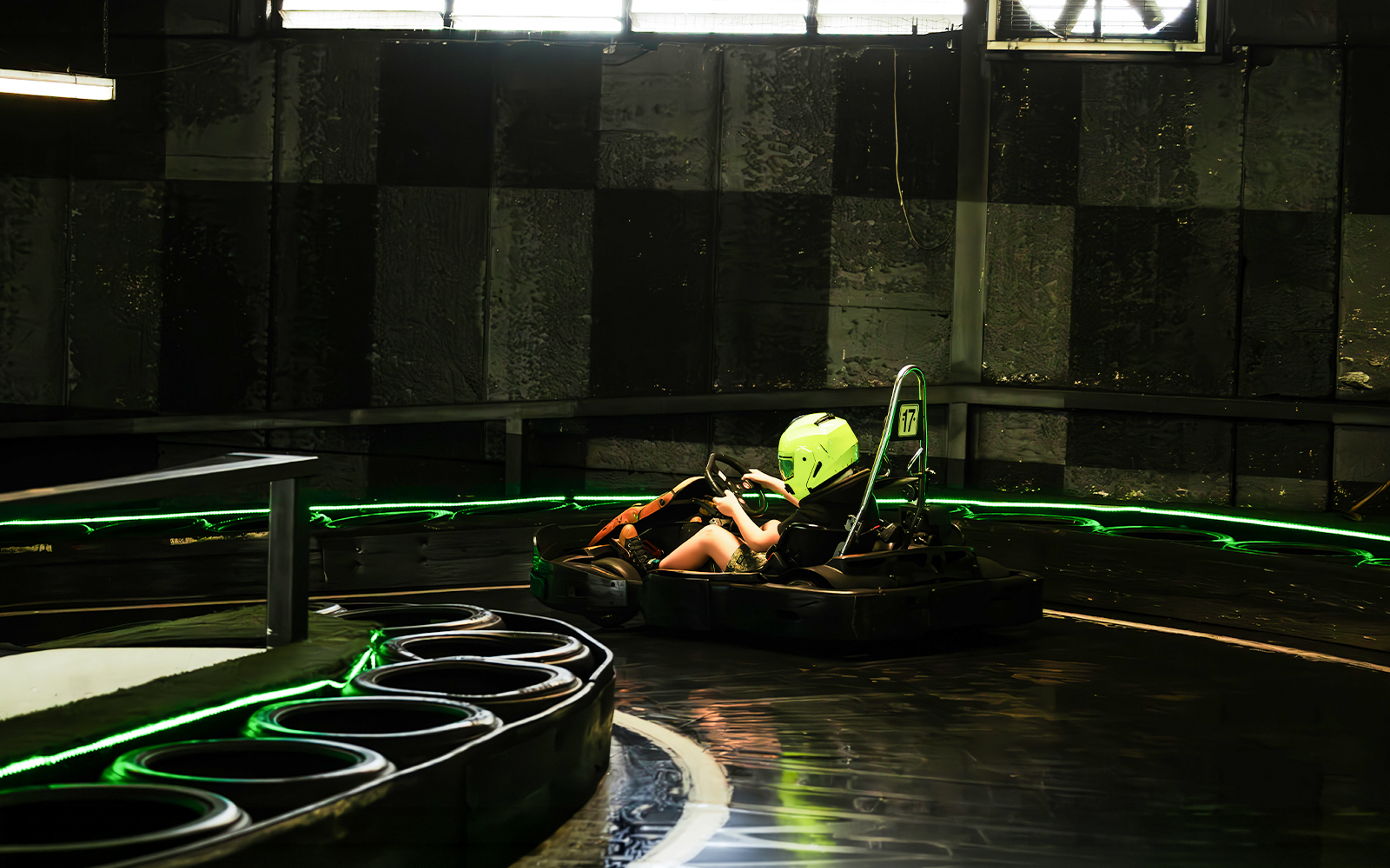 Indoor karting track with racer wearing a helmet navigating a curve.