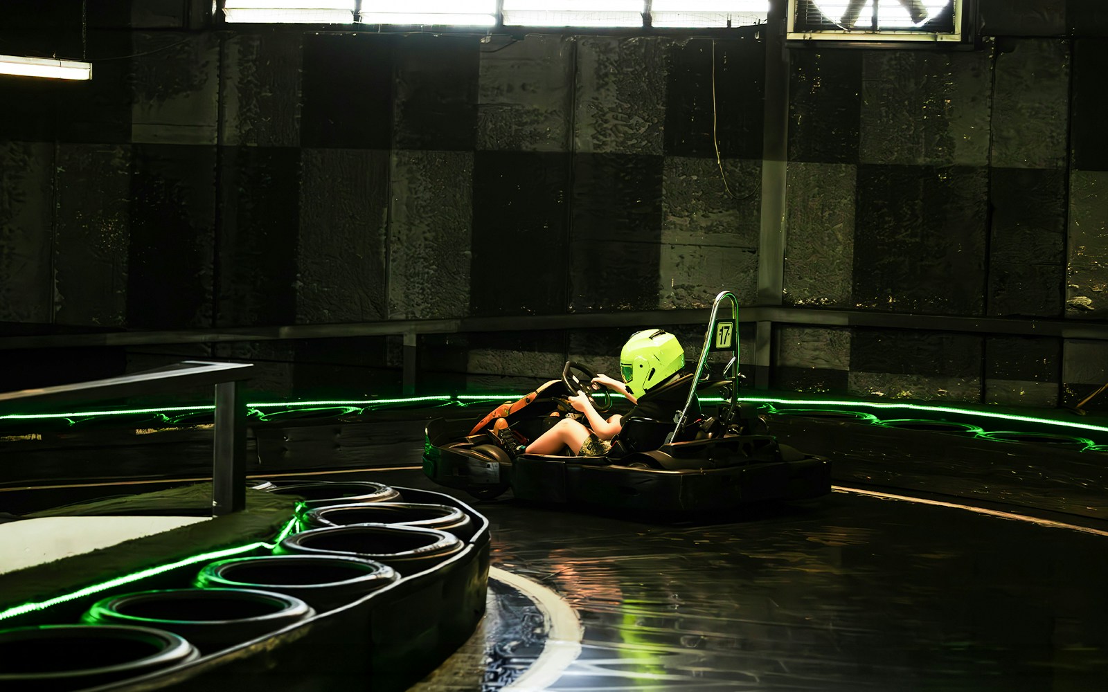 Indoor karting track with racer wearing a helmet navigating a curve.