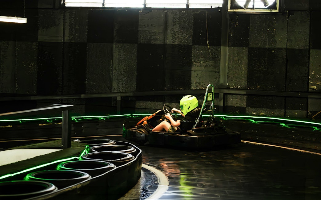 Indoor karting track with racer wearing a helmet navigating a curve.